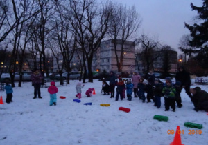 Dzieci z rodzicami stoją na śniegu przy rozstawionych pachołkach.